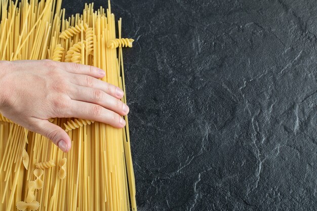 Female hands touching various pasta on dark surface.