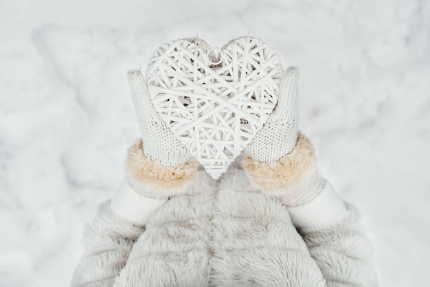 Female hands in white knitted mittens with a entwined vintage romantic white heart