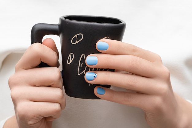 Female hands with blue nail design holding black coffee cup.