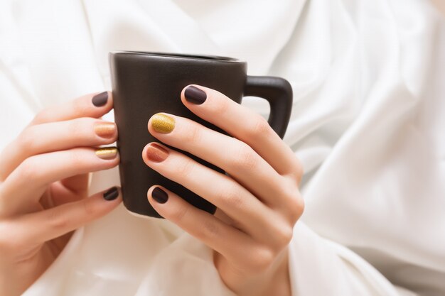 Female hands with brown nail design holding black cup.