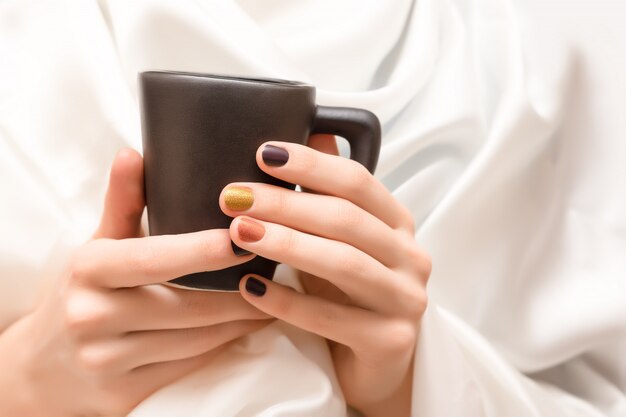 Female hands with brown nail design holding black cup.