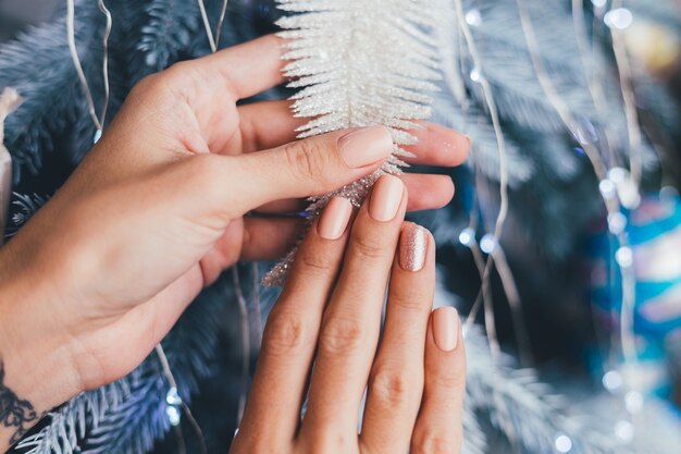 Female hands with Christmas new year nail design. Nude beige nail polish manicure, one finger shiny golden bronze