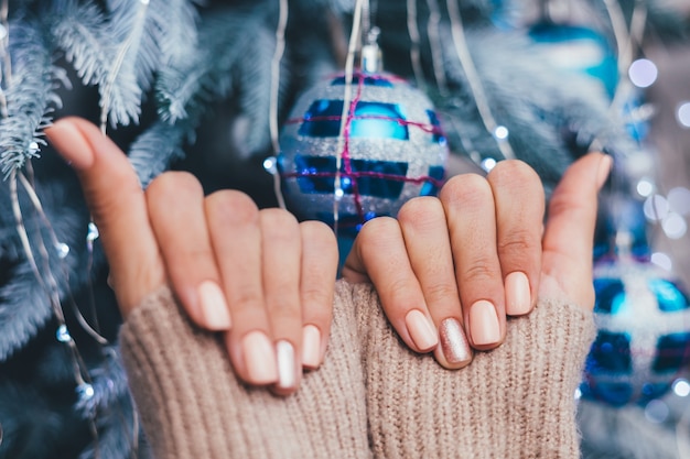 Женские руки с дизайном ногтей Рождество Новый год. Маникюр с лаком для ногтей телесного бежевого цвета, блестящая золотистая бронза на один палец