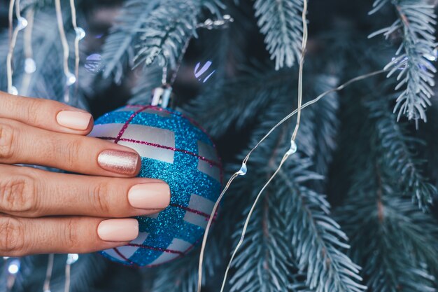 Female hands with Christmas new year nail design. Nude beige nail polish manicure, one finger shiny golden bronze