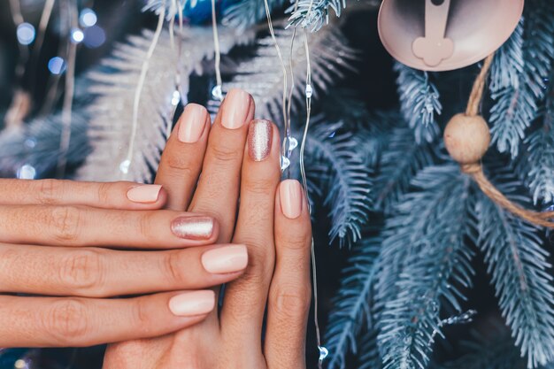 크리스마스 새 해 네일 디자인 여성 손. 누드 베이지 매니큐어 매니큐어, 한 손가락으로 반짝이는 황금색 청동