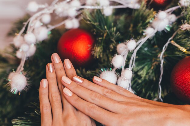 Female hands with Christmas new year nail design. Nude beige nail polish manicure