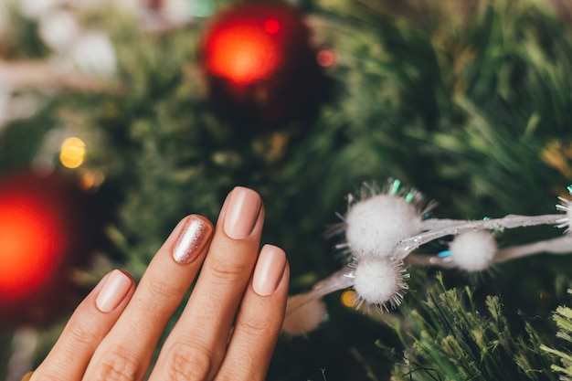 Женские руки с дизайном ногтей Рождество Новый год. Нюдовый бежевый маникюр с лаком