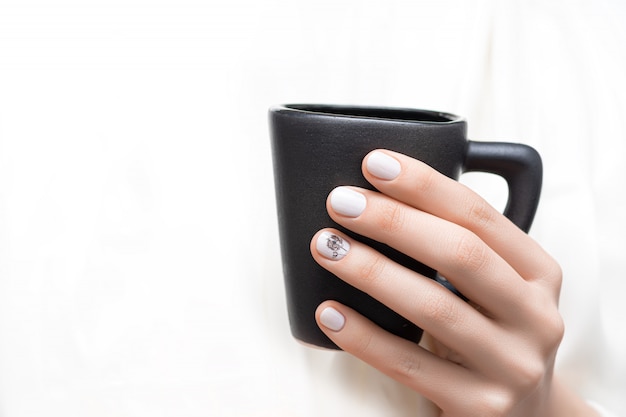 Female hands with white nail design holding black cup.