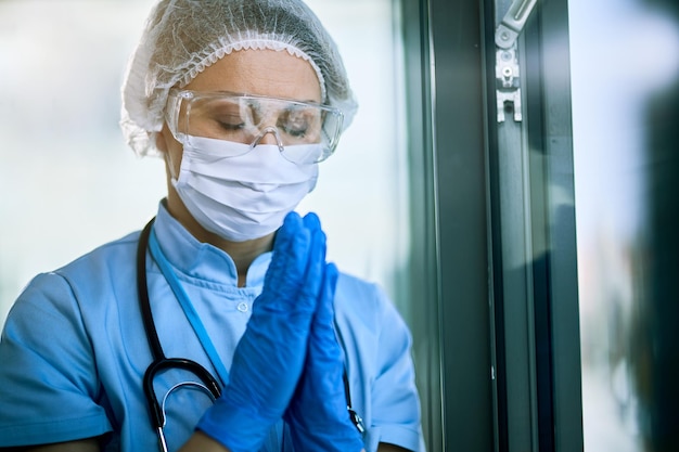 Female healthcare worker with hands clasped praying at medical clinic