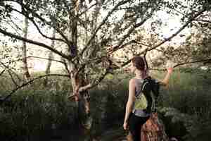 Foto gratuita viandante femminile con lo zaino che sta vicino all'albero