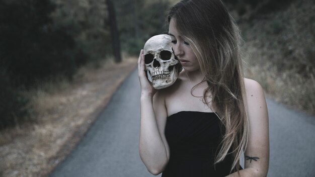 Female holding a artificial man skull on shoulder standing on road