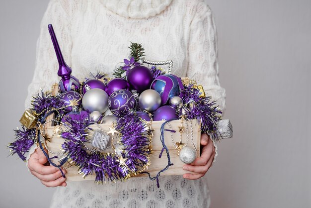 Женщина держит коробку, полную фиолетовых рождественских украшений
