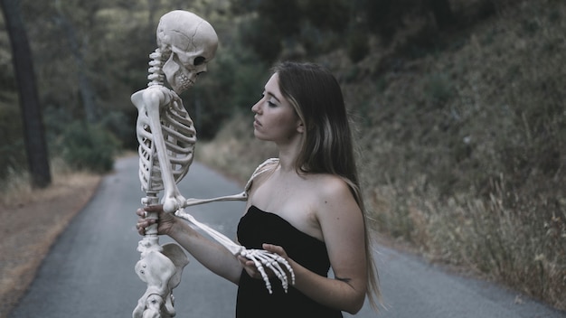 Free photo female holding decorative skeleton of man standing on road