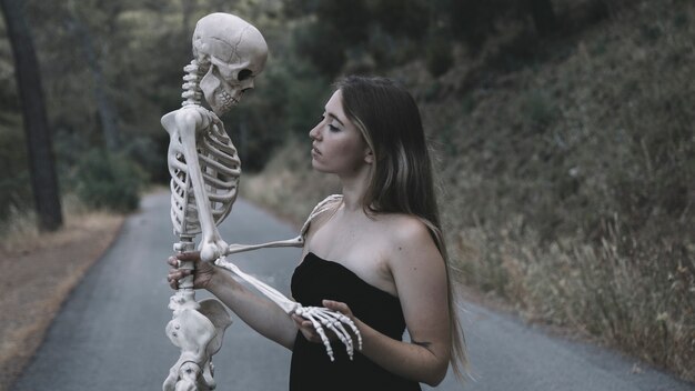 Female holding decorative skeleton of man standing on road