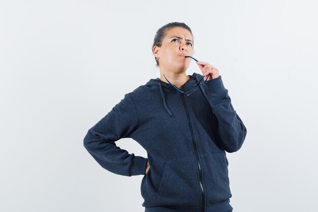 Female holding hand on mouth in hoodie and looking pensive , front view.