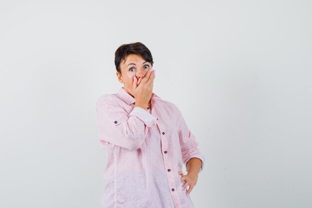 Female holding hand on mouth in pink shirt and looking surprised. front view.