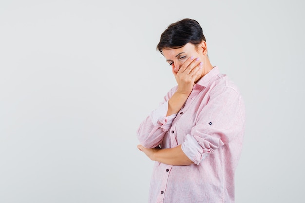 Female holding hand on mouth in pink shirt and looking upset. front view.