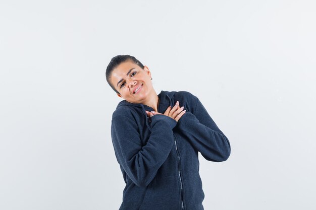 Female holding hands on chest in hoodie and looking cute , front view.