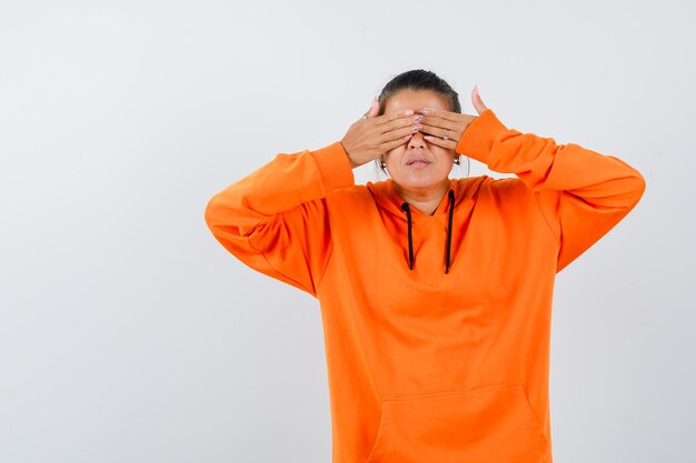 Female holding hands on eyes in orange hoodie and looking excited 