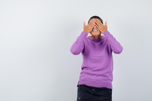 Female holding hands on eyes in wool blouse and looking excited 