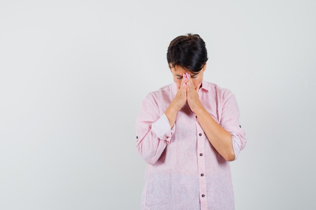 Free photo female holding hands in praying gesture in pink shirt and looking hopeful , front view.