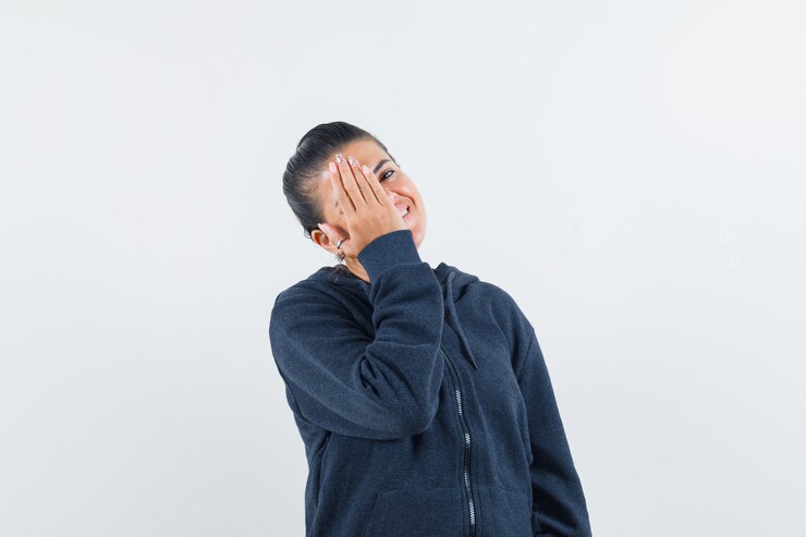 Free Photo female in hoodie holding hand on eye and looking happy , front view.