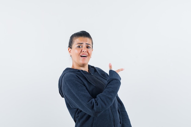 Female in hoodie pointing to the right side and looking confident , front view.