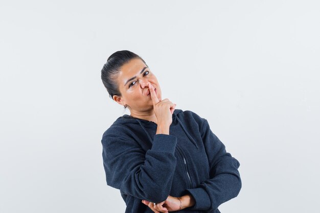 Female in hoodie showing silence gesture and looking confident , front view.