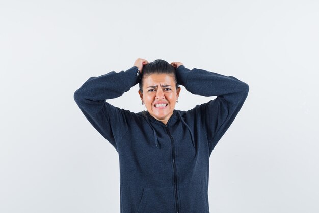 Female in hoodie tearing her hair and looking wistful , front view.