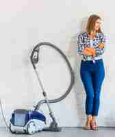 Free photo female housemaid standing near vacuum cleaner in front of brick wall