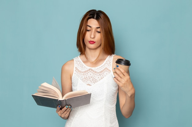 Бесплатное фото Женщина в белом платье держит чашку кофе и читает книгу