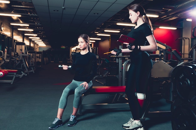 Female instructor giving training to young woman exercising with dumbbell