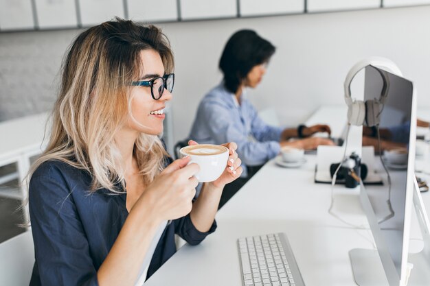 IT-специалист женщина смотрит на экран компьютера, попивая кофе с удовольствием