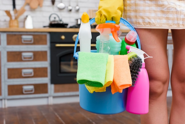 Female janitor holding cleaning accessories in bucket standing in kitchen