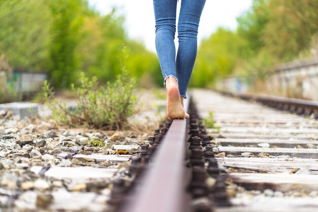 Female in jeans walking through the train rails barefoot