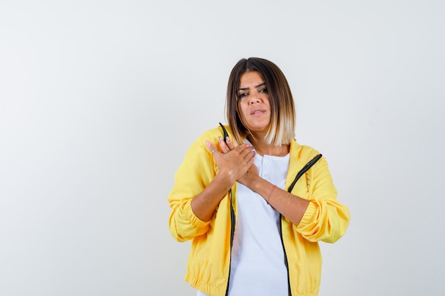 Tシャツ、ジャケット、悲しそうな正面図で胸に手を置いている女性。