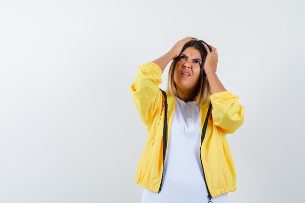 Female keeping hands on head in t-shirt, jacket and looking wistful , front view.