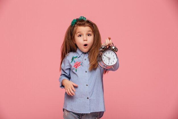 female kid posing with eyes and mouth wide open holding clock nearly 6 being shocked or shaken up