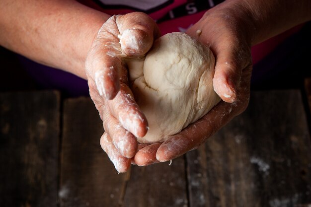 Female kneading dough in palms on wooden table, close-up.