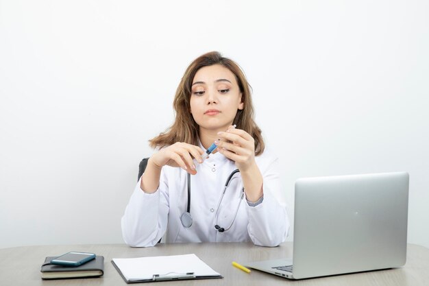 Female laboratory researcher sitting at the desk with syringe . High quality photo