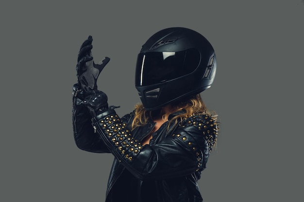 Female in leather clothes, moto gloves and safety helmet on a grey background.