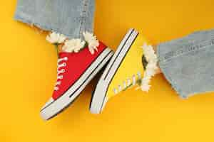 Free photo female legs in sneakers with flowers on yellow background