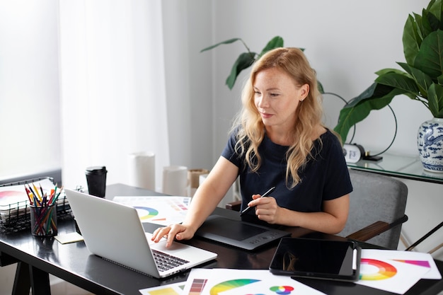 Женский дизайнер логотипов работает над своим планшетом, подключенным к ноутбуку