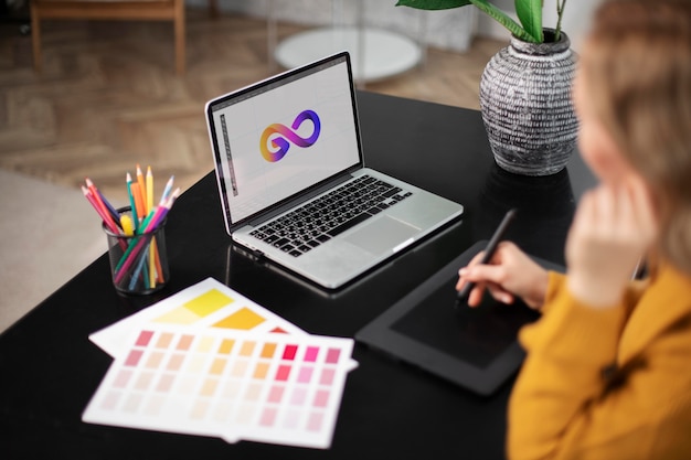 Designer di logo femminile che lavora sul suo tablet collegato a un laptop