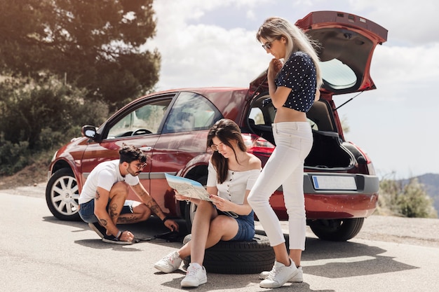 Female looking at map near the man examining the broken down car