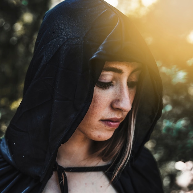 Female magician in black cape in sunny forest