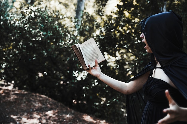 Female magician reading spell in thicket