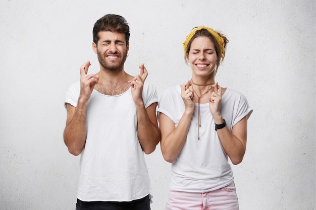 Female and male closing their eyes crossing fingers with hope while anticipating important news