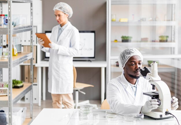 현미경과 태블릿을 사용하는 생명 공학 실험실의 여성 및 남성 연구원