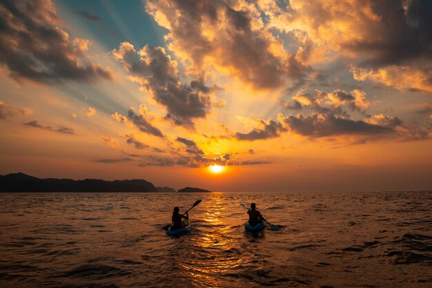 Female and a male sailing with canoes close to each other at sunset